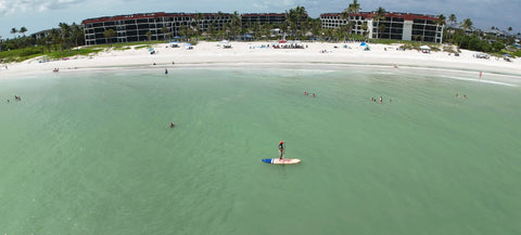 Paddleboarder off a Sanibel Island Gulf beach with resort accommodation along the shoreline